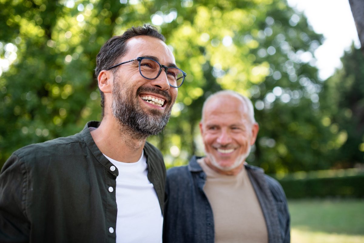 A man and an older man smile side by side as they walk in the park.